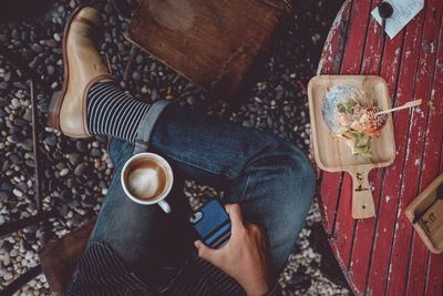 High angle view of man holding mobile phone while having coffee