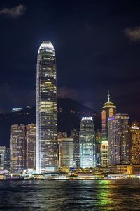 Illuminated buildings by river against sky in city at night