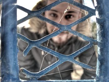 Close-up portrait of man seen through fence during winter