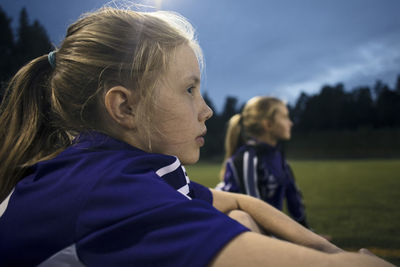 Side view of girl sitting at soccer field against sky