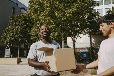 Smiling male volunteer passing donation box to teammate during charity drive at community center