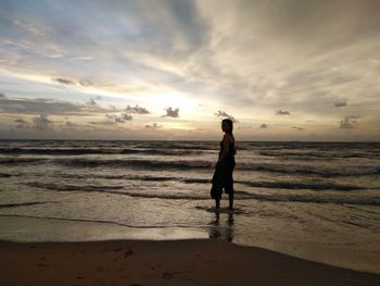 Woman standing at beach against sky during sunset