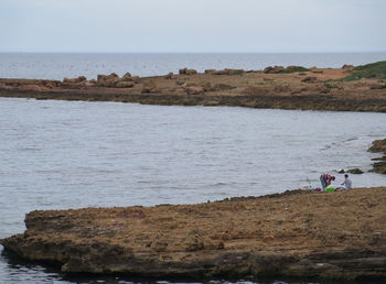 People on rocks by sea against sky