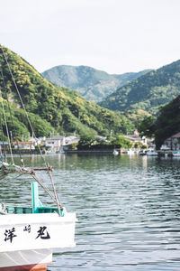 Boats sailing on river by mountains against clear sky