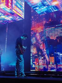 Rear view of man standing against illuminated city at night