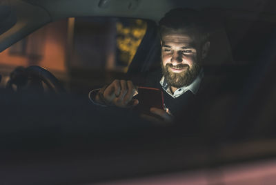 Smiling businessman using cell phone in car at night