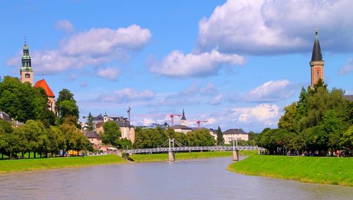 View of buildings by river against cloudy sky