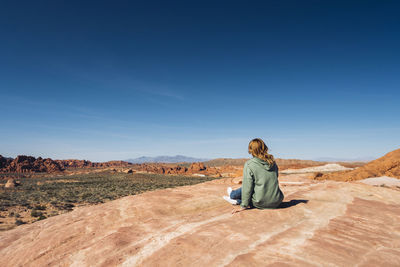 Man sitting on rock in desert against blue sky