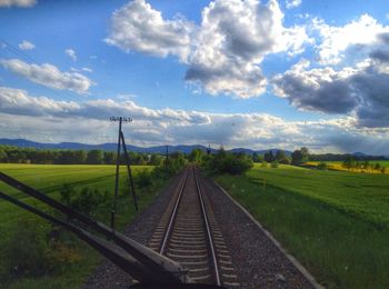 Road passing through field against cloudy sky