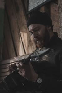 Young man playing guitar while sitting against wall