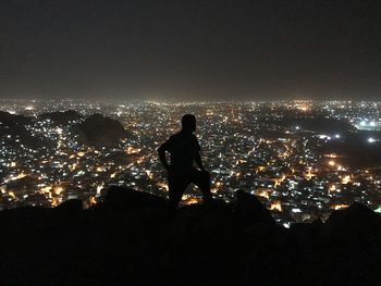 Silhouette man standing by illuminated cityscape against sky at night