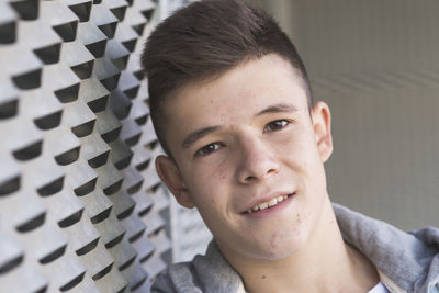 Portrait of teenage boy smiling while standing by metal wall