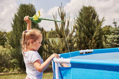 Cute girl holding fishing rod standing by wading pool