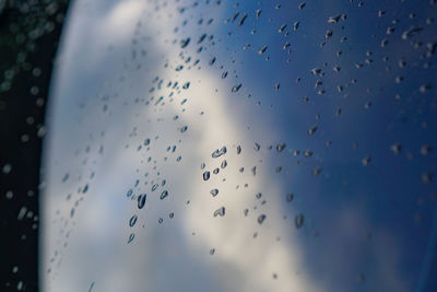 Low angle view of wet glass window against blue sky