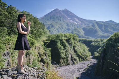 Full length of woman looking away while standing on rock against mountains and sky