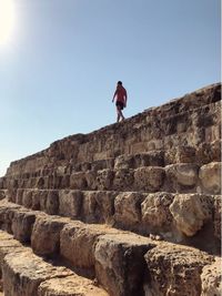 Low angle view of man standing on rock against clear blue sky