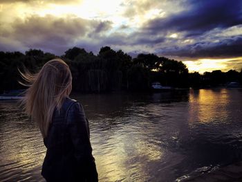 Rear view of woman standing by river during sunset