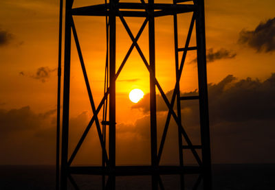 Silhouette built structure by sea against orange sky