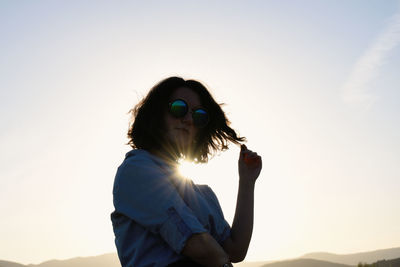 Midsection of woman with sunglasses against sky during sunset