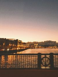 Illuminated bridge over river against sky in city