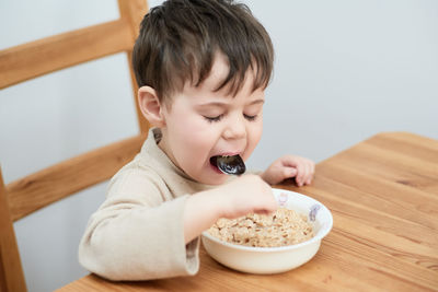 Little boy eating oatmeal for breakfast in the kitchen