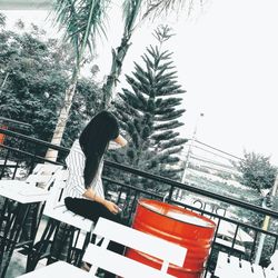 Side view of person sitting by swimming pool against sky