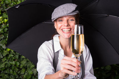 Portrait of woman with umbrella holding champagne flute at backyard