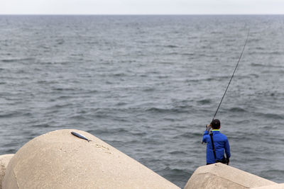 Rear view of woman standing on rock while fishing at sea