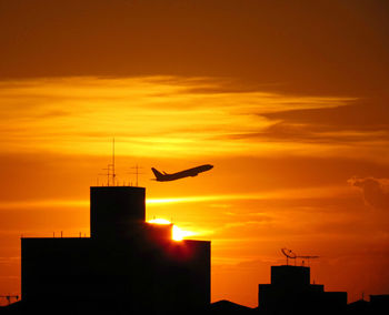 Silhouette birds flying against orange sky