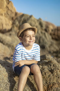 Cute boy wearing hat sitting on rock