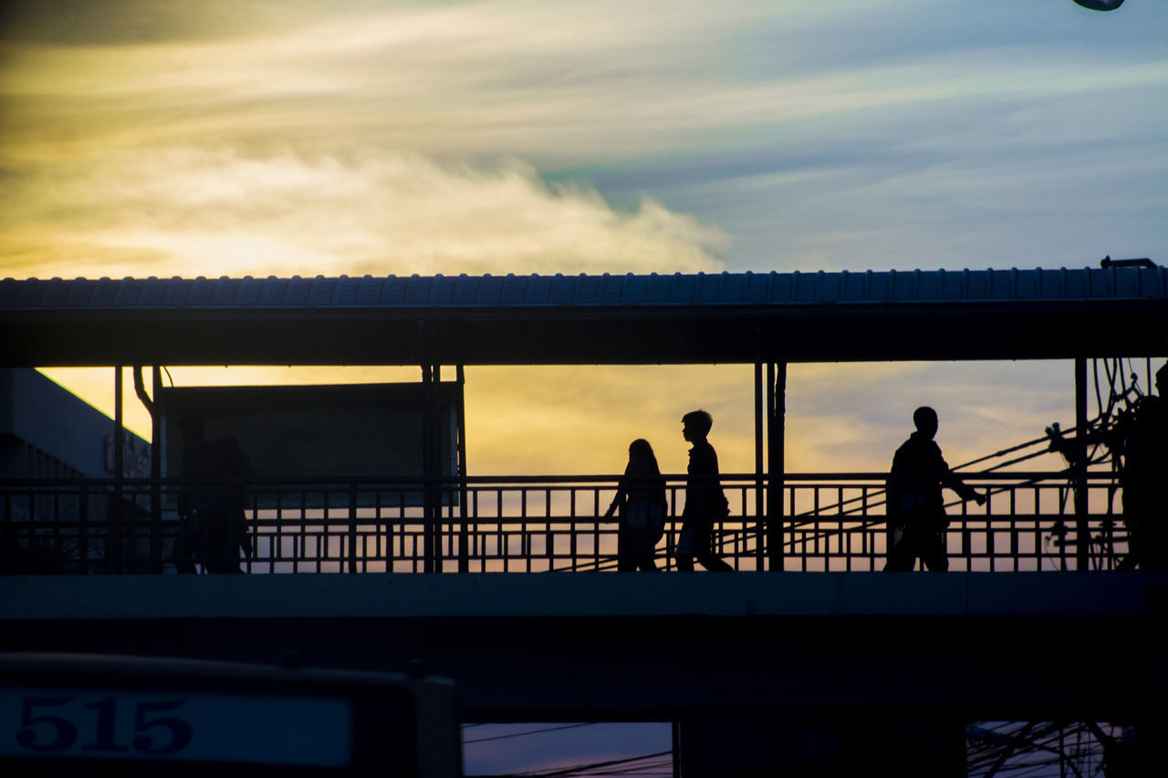 SILHOUETTE PEOPLE STANDING ON RAILING AGAINST SKY AT SUNSET