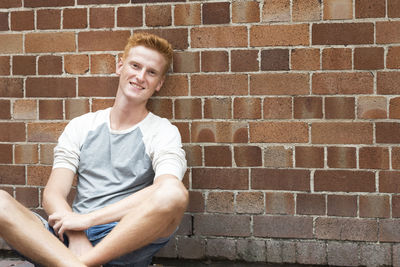 Portrait of a smiling young woman sitting on brick wall