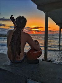 Woman sitting on beach against sky during sunset