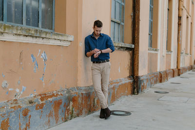 Full length man checking time while leaning on building