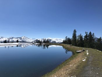 Scenic view of lake by snowcapped mountains against clear blue sky