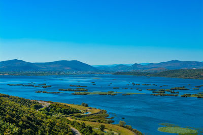 Scenic view of lake and mountains against clear blue sky