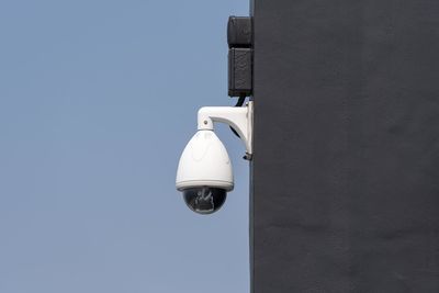Low angle view of security camera on building against clear blue sky during sunny day