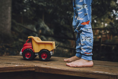 Low section of child standing by toy car on wooden floor