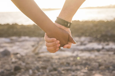 Cropped image of couple holding hands at beach during sunset