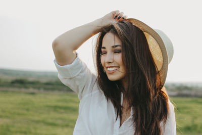 Woman holding hat against landscape and sky