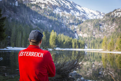 Rear view of man standing by lake against mountain