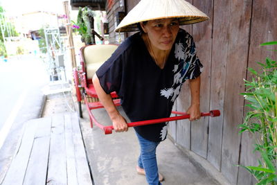 Mature woman wearing asian style conical hat while pulling rickshaw in city