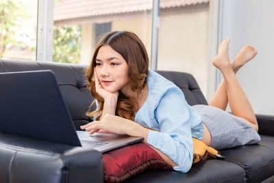 Young woman using mobile phone while sitting on sofa at home