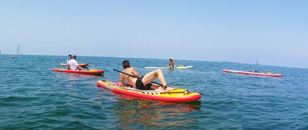 People lying on paddleboards in sea against clear sky