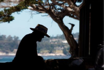 Silhouette man wearing hat sitting on log