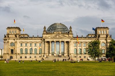 People at reichstag building against cloudy sky