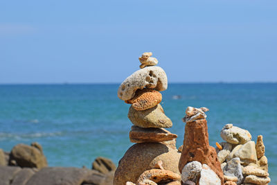 Stack of stones on rock by sea against sky
