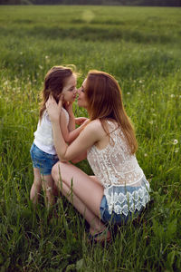 Mom and daughter are sitting in a green field in white t-shirt