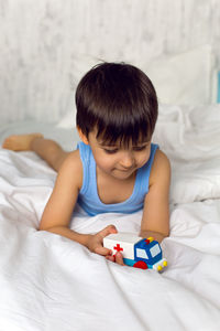 Child plays with a wooden ambulance toy on the bed 