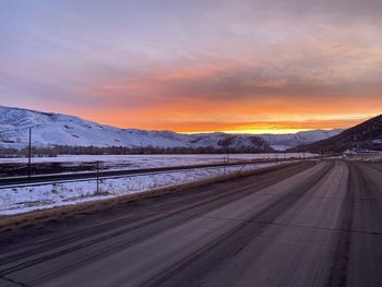 Road by snowcapped mountains against sky during sunset